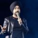 Diljit Dosanjh kicks off his Aura World Tour at BC Place on April 23, 2026, in Vancouver, British Columbia, Canada. He is wearing a black jacket over a black t-shirt and sporting a black turban, as he speaks on a microphone from the stage.