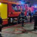Firefighters in blue uniforms stand in front of fire trucks