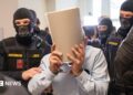 Ex-Syrian intelligence chief Khaled al-Halabi (C) covers his face as he is escorted in handcuffs to the courtroom by justice officers for the trial at the Regional Vienna's Court of Austria.
