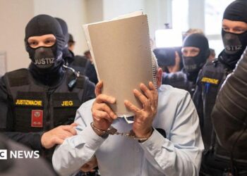 Ex-Syrian intelligence chief Khaled al-Halabi (C) covers his face as he is escorted in handcuffs to the courtroom by justice officers for the trial at the Regional Vienna's Court of Austria.