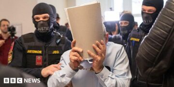 Ex-Syrian intelligence chief Khaled al-Halabi (C) covers his face as he is escorted in handcuffs to the courtroom by justice officers for the trial at the Regional Vienna's Court of Austria.