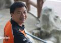 Wang Jibing in an orange polo shirt smiling at the camera