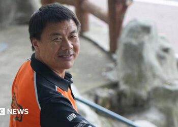 Wang Jibing in an orange polo shirt smiling at the camera
