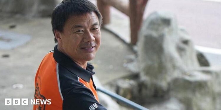 Wang Jibing in an orange polo shirt smiling at the camera