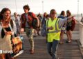 A volunteer gives indication to holidaymakers from Lege-Cap-Ferret upon their arrival in Arcachon by boat during an evacuation operation of the entire Cap-Ferret peninsula, in southwestern France, on July 24, 2026 whilst a wildfire is spreading across the area