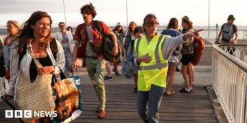 A volunteer gives indication to holidaymakers from Lege-Cap-Ferret upon their arrival in Arcachon by boat during an evacuation operation of the entire Cap-Ferret peninsula, in southwestern France, on July 24, 2026 whilst a wildfire is spreading across the area