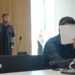 A man holds a sheet of paper over his face, wearing a black shirt in court