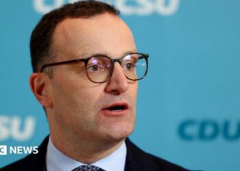 Jens Spahn speaks with German media during a party meeting, he is wearing a black suit and black glasses.