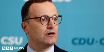Jens Spahn speaks with German media during a party meeting, he is wearing a black suit and black glasses.