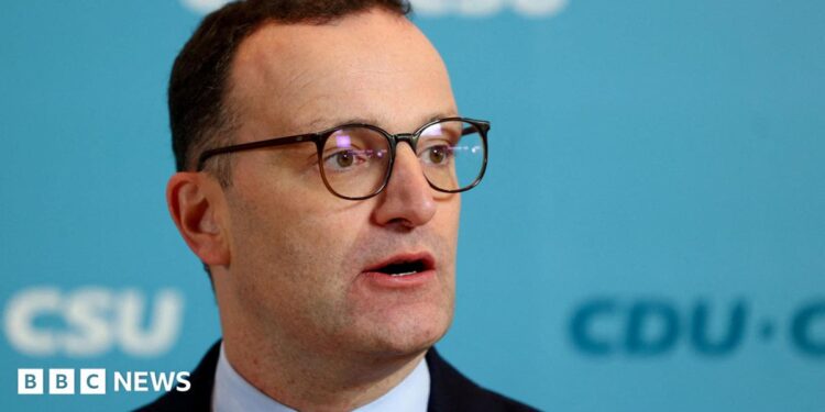 Jens Spahn speaks with German media during a party meeting, he is wearing a black suit and black glasses.