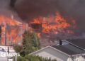 Several houses on fire engulfed in dark smoke, with untouched houses in front of them