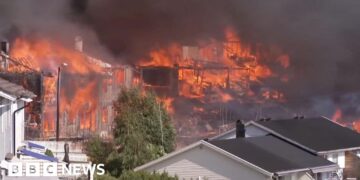 Several houses on fire engulfed in dark smoke, with untouched houses in front of them