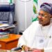 Prince Adeniyi Adeyemi Matthew, PFIPC's director general, sits in an office. He is wearing a white gown, glasses and a grey and pink cap