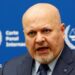 International Criminal Court Prosecutor Karim Khan speaks during an interview while sitting in front of a blue sign with blurry white writing and the symbol of the ICC - the scales of justice surrounded by a laurel wreath.