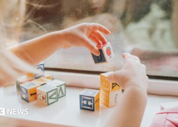 A child plays with letter blocks in front of a window