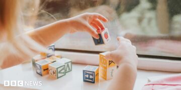 A child plays with letter blocks in front of a window