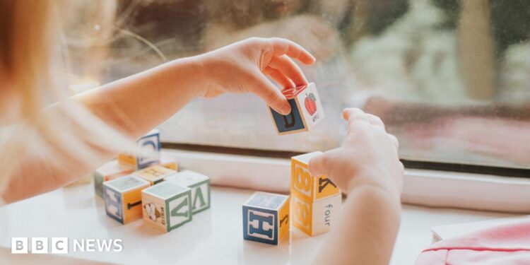 A child plays with letter blocks in front of a window