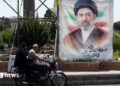 A man and a woman on a motorcycle pass a large portrait of Supreme Leader Ayatollah Mojtaba Khamenei on a street in Tehran.