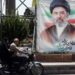 A man and a woman on a motorcycle pass a large portrait of Supreme Leader Ayatollah Mojtaba Khamenei on a street in Tehran.