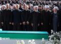Iranian President Masoud Pezeshkian, Iran's Parliament speaker Mohammad Baqer Qalibaf and Chief Justice of Iran Gholam-hossein Mohseni Ejei with officials attend a prayer during a public farewell ceremony to pay their respects to late Supreme Leader Ayatollah Ali Khamenei. A large crowd can be seen in the background as everyone stands looking at the coffin