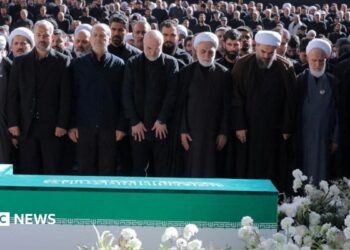 Iranian President Masoud Pezeshkian, Iran's Parliament speaker Mohammad Baqer Qalibaf and Chief Justice of Iran Gholam-hossein Mohseni Ejei with officials attend a prayer during a public farewell ceremony to pay their respects to late Supreme Leader Ayatollah Ali Khamenei. A large crowd can be seen in the background as everyone stands looking at the coffin