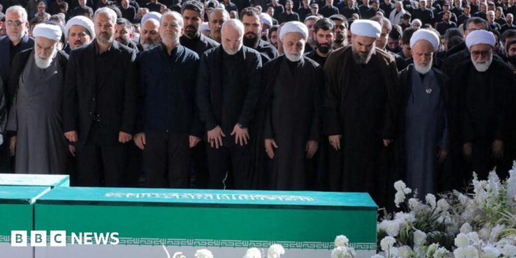 Iranian President Masoud Pezeshkian, Iran's Parliament speaker Mohammad Baqer Qalibaf and Chief Justice of Iran Gholam-hossein Mohseni Ejei with officials attend a prayer during a public farewell ceremony to pay their respects to late Supreme Leader Ayatollah Ali Khamenei. A large crowd can be seen in the background as everyone stands looking at the coffin
