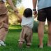 A young toddler is led away by his parents, who are holding each of his hands