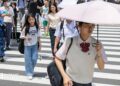 Japanese school girl with an umbrella walks over a crossroad on a summer day