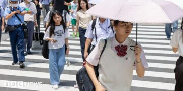 Japanese school girl with an umbrella walks over a crossroad on a summer day