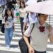 Japanese school girl with an umbrella walks over a crossroad on a summer day