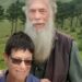 Rodney Saunders stands behind Rachel. Rodney has a long grey beard while Rachel has dark hair and is wearing sunglasses
