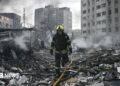 Sarah Rainsford in a brown shirt with short sleeves in front of rubble in Kyiv