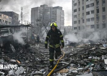 Sarah Rainsford in a brown shirt with short sleeves in front of rubble in Kyiv