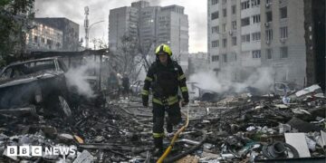 Sarah Rainsford in a brown shirt with short sleeves in front of rubble in Kyiv