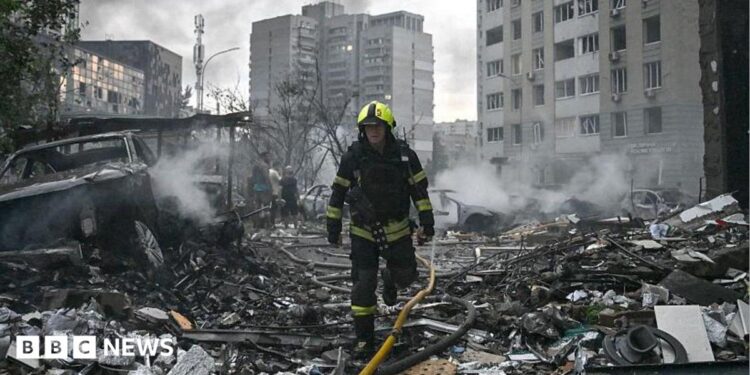 Sarah Rainsford in a brown shirt with short sleeves in front of rubble in Kyiv