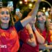A female celebrates her country's World Cup win with her hands raised in a crowd full of Spanish supporters.
