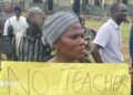 A woman holds up a banner at a protest at a school.
