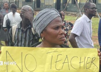 A woman holds up a banner at a protest at a school.