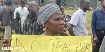 A woman holds up a banner at a protest at a school.