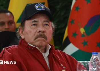 President of Nicaragua Daniel Ortega looks on during the opening event of the XXIII Summit of the Bolivarian Alliance for the Americasin Caracas, Venezuela, in 2024. He is wearing a red jacket and a baseball cap with the Nicaraguan flag emblazoned on it. He has a moustache.