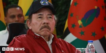 President of Nicaragua Daniel Ortega looks on during the opening event of the XXIII Summit of the Bolivarian Alliance for the Americasin Caracas, Venezuela, in 2024. He is wearing a red jacket and a baseball cap with the Nicaraguan flag emblazoned on it. He has a moustache.