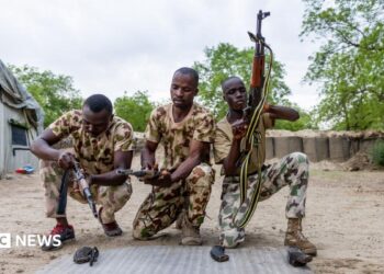 Three Nigerian soldiers wearing army fatigues appear to load their guns