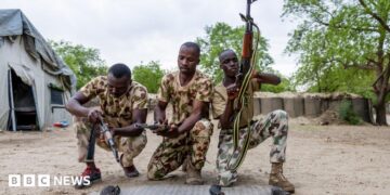 Three Nigerian soldiers wearing army fatigues appear to load their guns