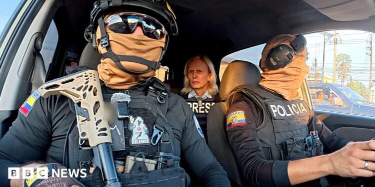 Two Ecuadoran police officers in dark sunglasses, helmets and balaclavas - which entirely obscure their faces - sit in a car in front of the BBC's Orla Guerin, wearing a flak jacket with the word "PRESS" on it.