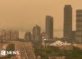 Orange haze fills the sky over a skyline of tall buildings and a highway in Toronto.