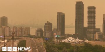 Orange haze fills the sky over a skyline of tall buildings and a highway in Toronto.