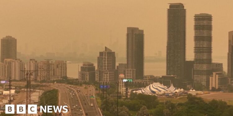 Orange haze fills the sky over a skyline of tall buildings and a highway in Toronto.