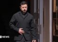 Zelensky, wearing a dark suit, walking through a doorway