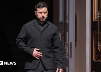 Zelensky, wearing a dark suit, walking through a doorway