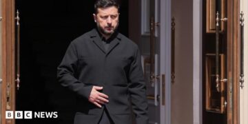 Zelensky, wearing a dark suit, walking through a doorway
